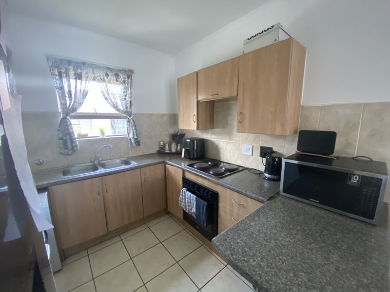 A functional kitchen featuring light wood-finish cabinetry, laminate countertops, a double sink, and a built-in electric oven and hob with tiled backsplash.