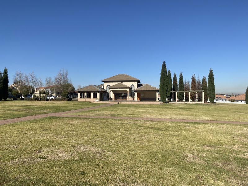 A wide-angle view of the rear exterior of the townhouse, featuring a large lawn, paved pathways, and a pergola structure.