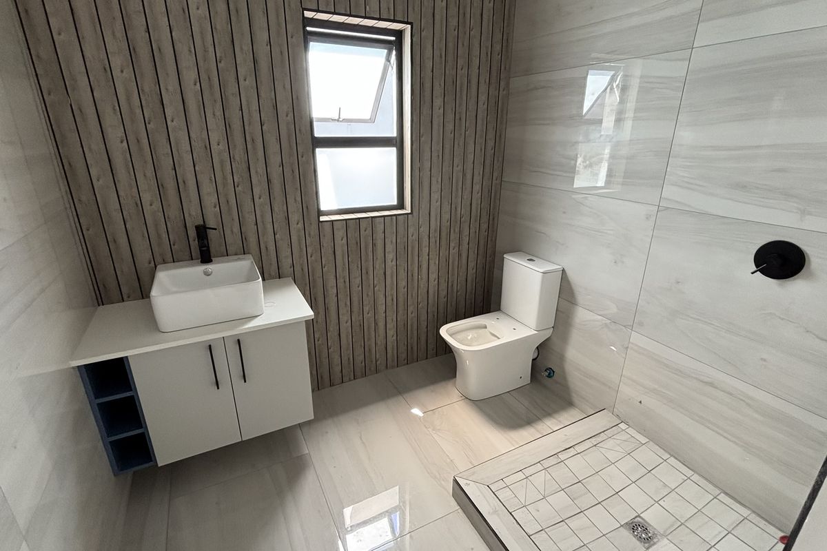Modern bathroom featuring a floating vanity with vessel sink, walk-in shower with tiled base, and contemporary wall paneling.