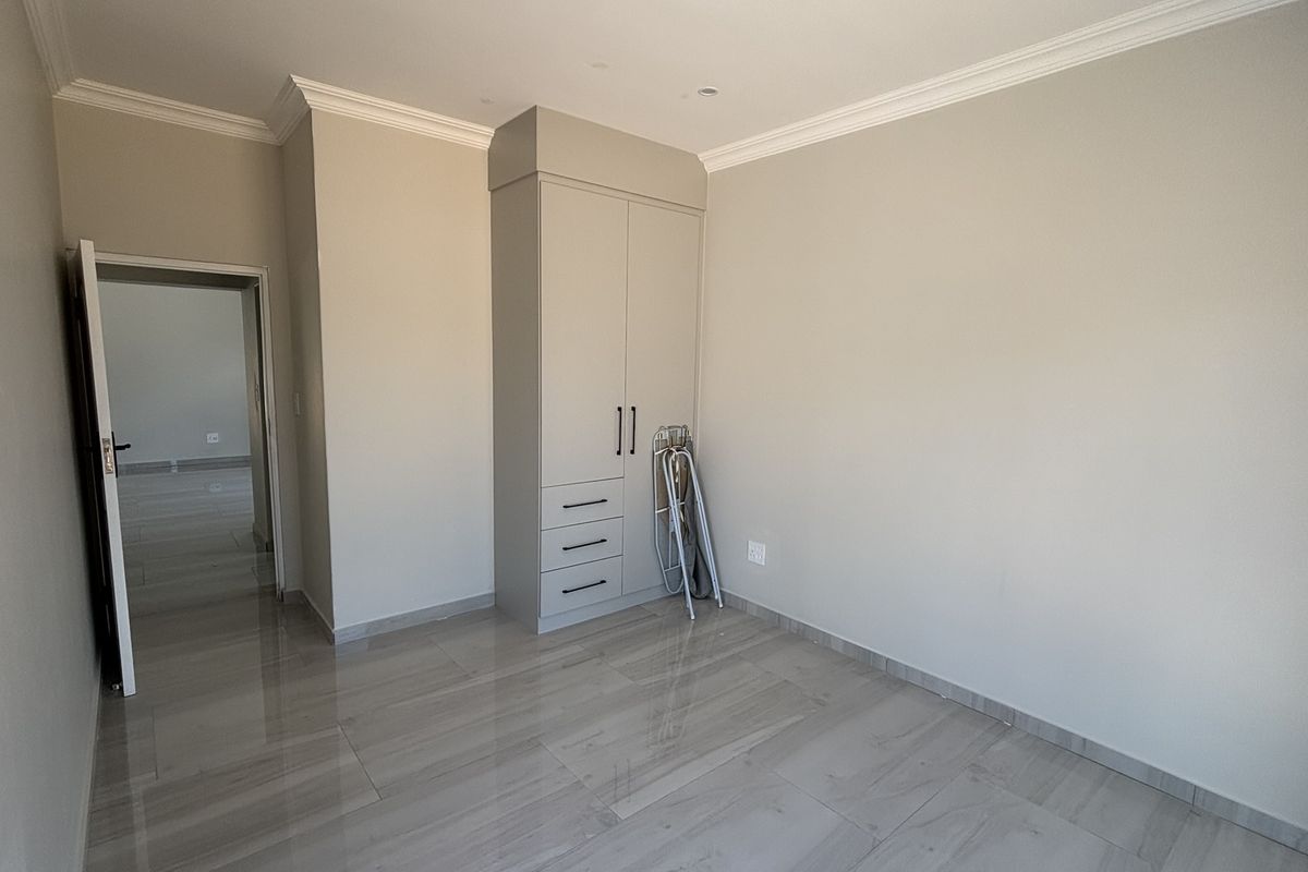 A bright, empty bedroom featuring neutral walls, polished tile flooring, and a built-in wardrobe with integrated drawers.