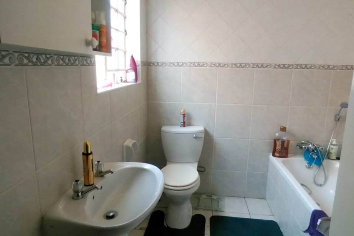 A functional bathroom featuring a standard bathtub, pedestal basin, and toilet with neutral wall tiling.