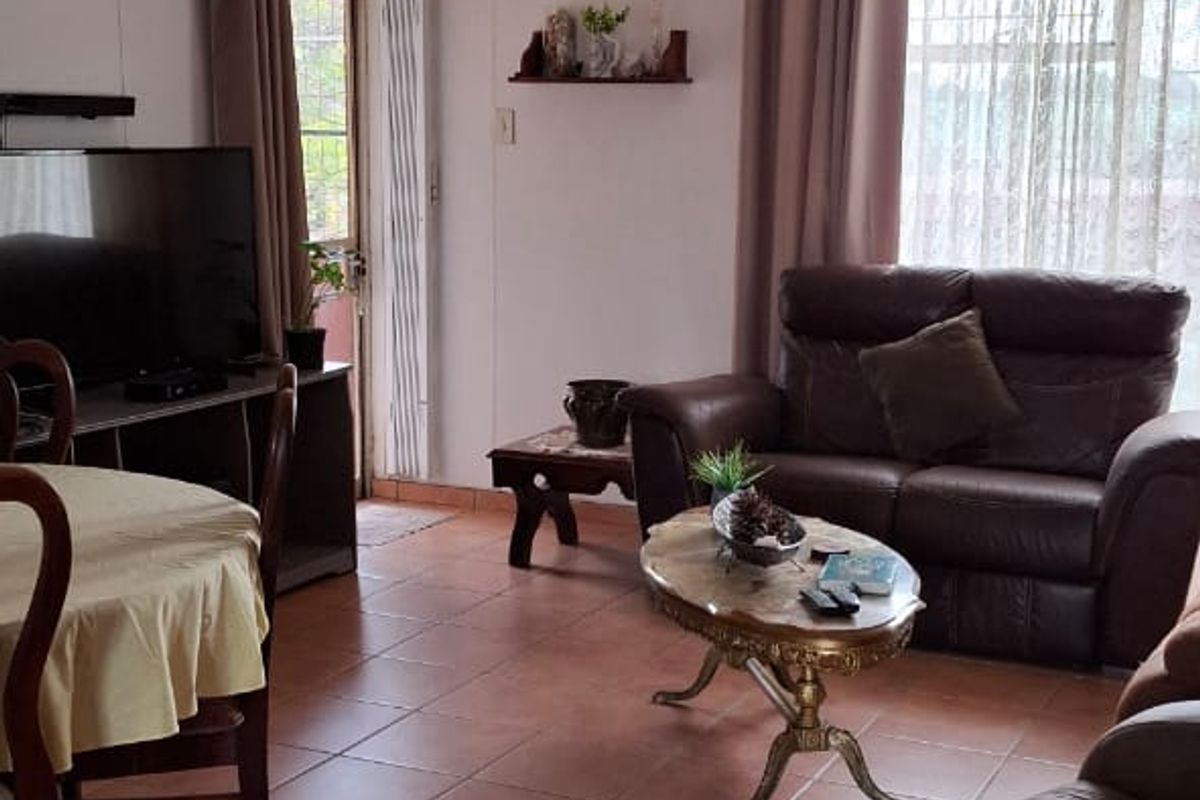 A living room area featuring tiled flooring, large windows with curtains, and access to an outdoor space.