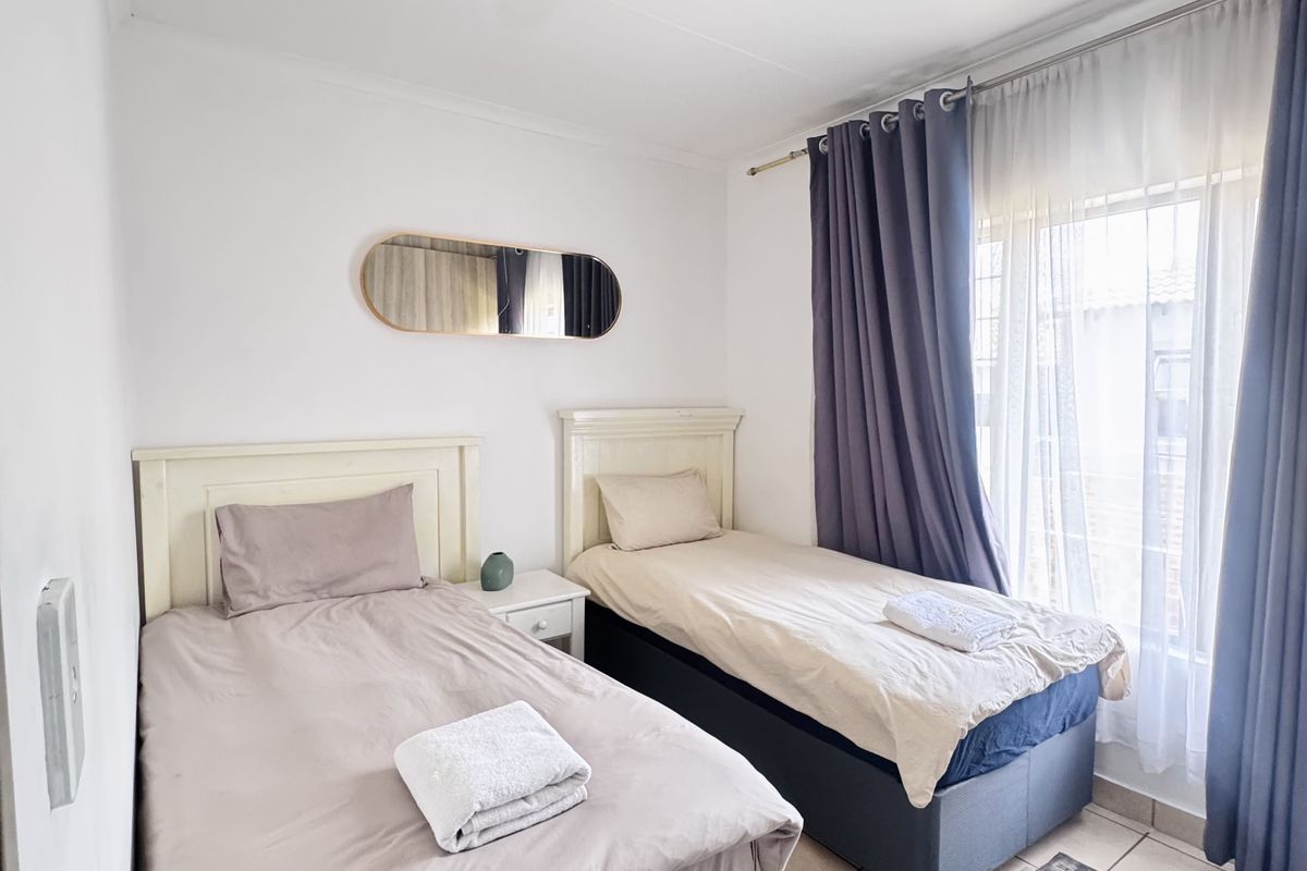 A bright bedroom featuring tiled flooring, a large window with curtain tracks, and a central ceiling light fixture.
