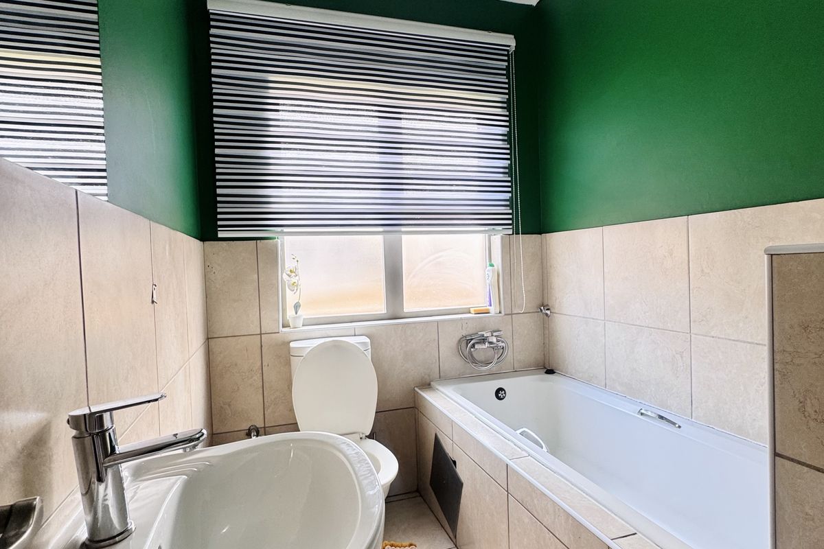 A compact bathroom featuring a pedestal basin, a standard bathtub with tiled surround, and a window with a roller blind.