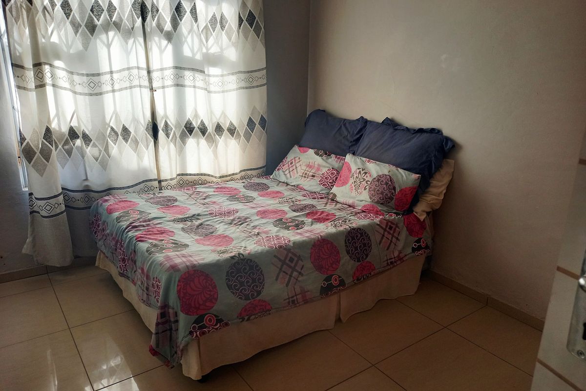 A bedroom featuring tiled flooring and a window dressed with patterned curtains.