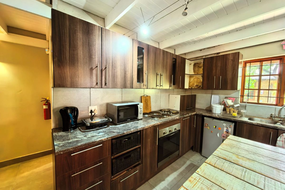 A functional kitchen featuring dark wood-finish cabinetry, granite-style countertops, a built-in oven, and a hob, set under a white exposed-beam ceiling.