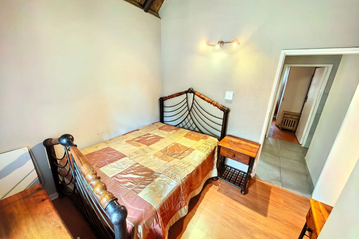A cozy bedroom featuring a high vaulted thatched ceiling, laminate flooring, and a wall-mounted light fixture, with direct access to an adjacent hallway.