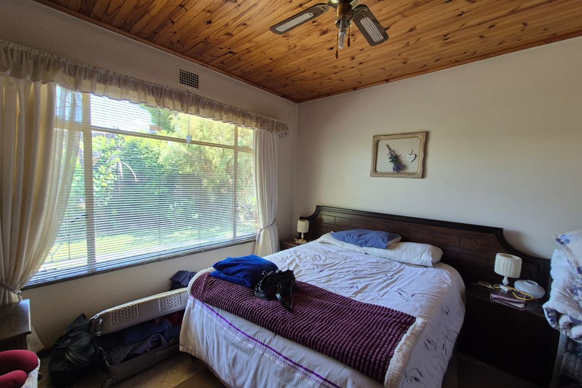 A bedroom featuring a large window with natural light, a timber-paneled ceiling, and a ceiling fan.