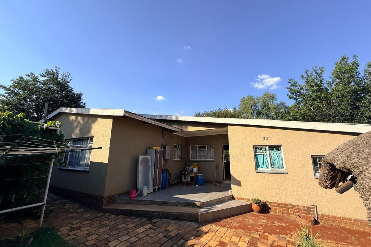 Rear view of the house featuring a covered patio area, paved courtyard, and exterior access to the property.