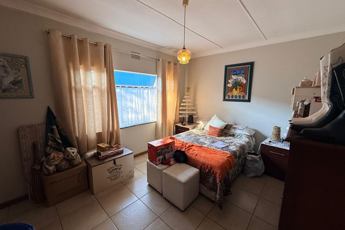 A functional bedroom featuring tiled flooring, a central pendant light, and a window with curtain tracks.