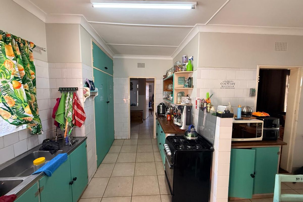 A dated kitchen featuring teal cabinetry, tiled splashbacks, tiled flooring, and a freestanding stove, offering a functional layout with potential for modernization.