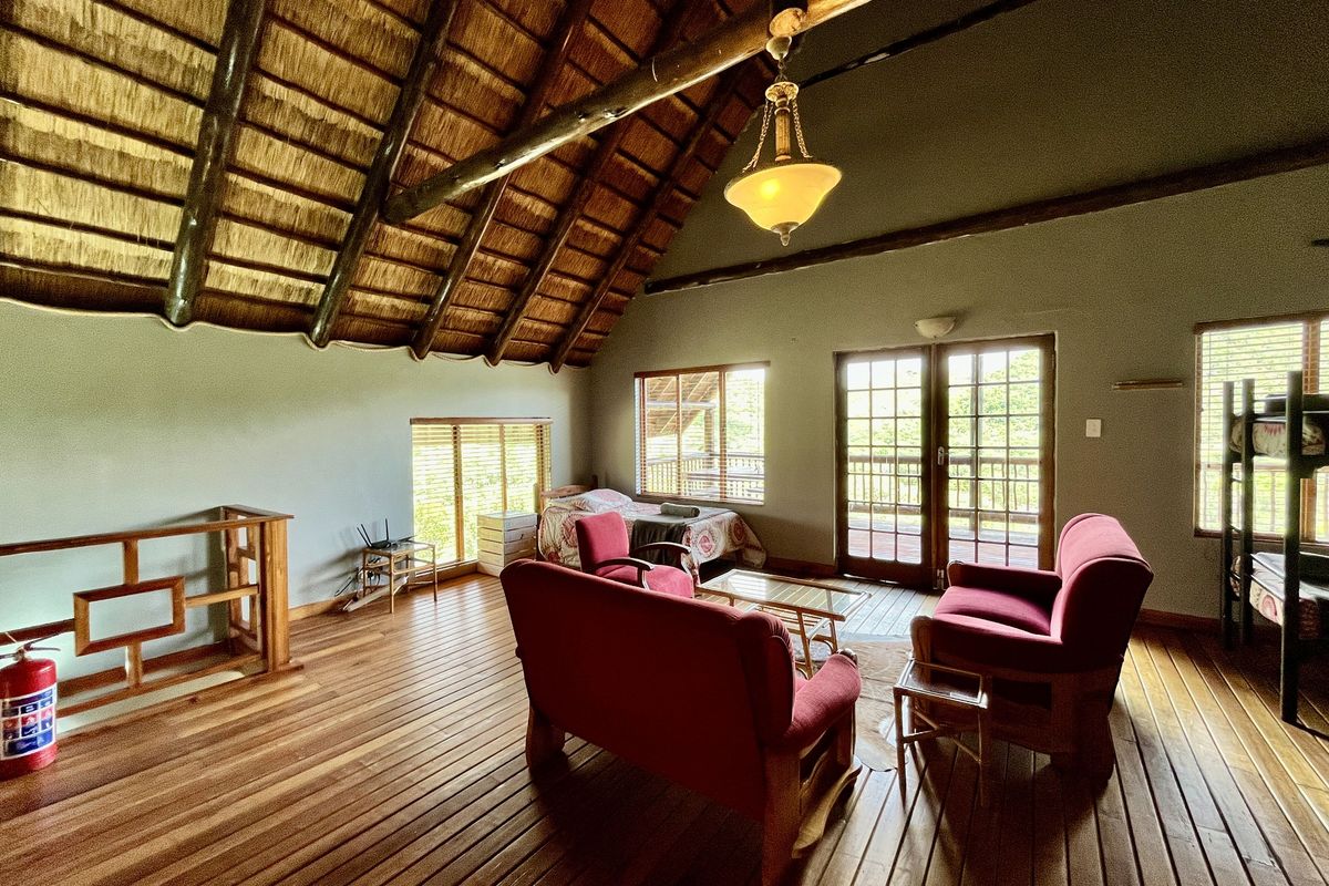 Spacious loft living area featuring a high vaulted thatched roof, exposed timber beams, polished wooden flooring, and direct access to a balcony.