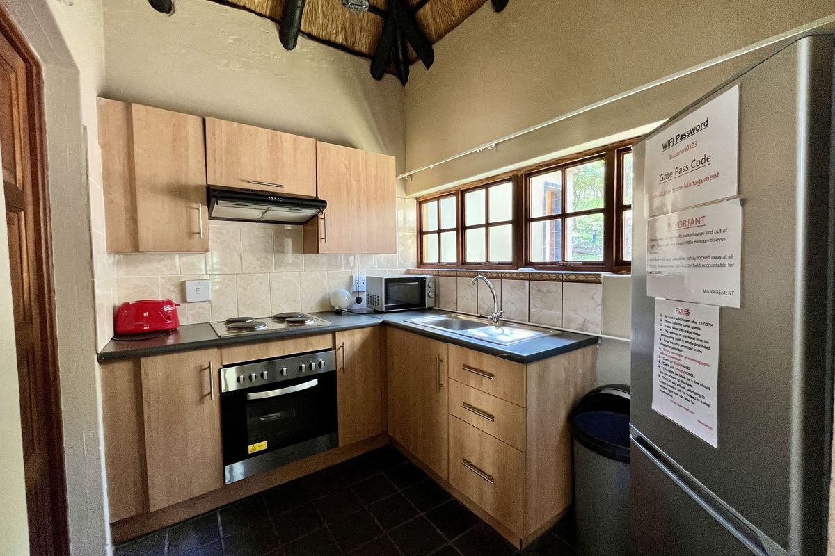 Compact kitchen featuring light wood cabinetry, built-in oven, electric hob, extractor fan, and tiled flooring under a traditional thatched roof structure.
