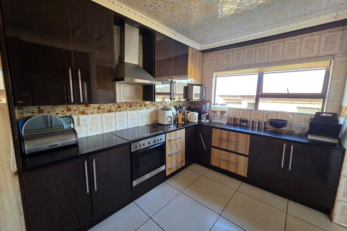 A functional kitchen featuring dark cabinetry, integrated oven and hob, extractor fan, and tiled flooring with a large window for natural light.
