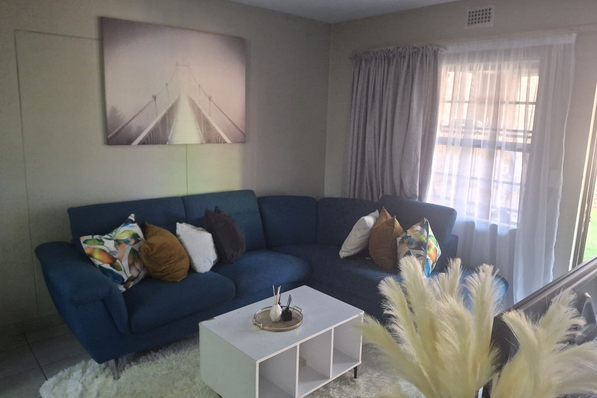 A comfortable living room featuring tiled flooring, neutral wall tones, and a large window with curtain treatments, providing natural light to the space.
