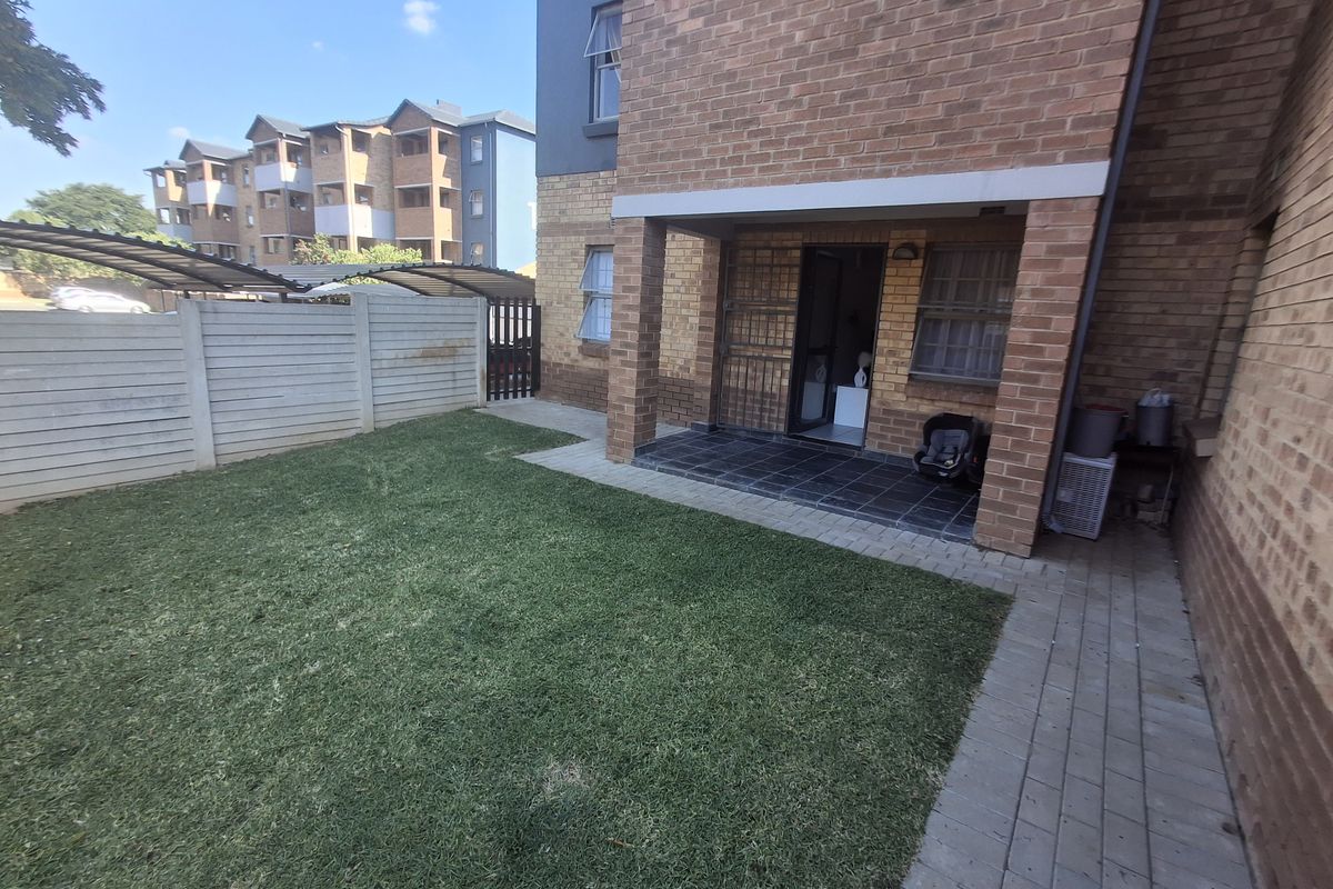 A private ground-floor garden area featuring a paved patio, brick facade, and a small lawn enclosed by a precast concrete boundary wall.
