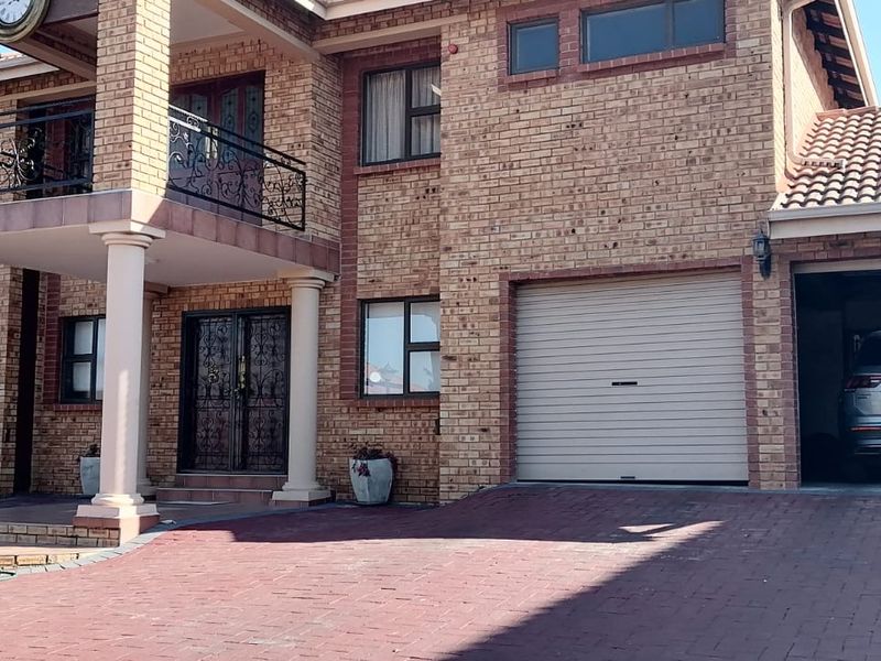 A well-maintained double-story brick apartment building featuring a paved driveway, double garage, and a decorative balcony with wrought iron railings.