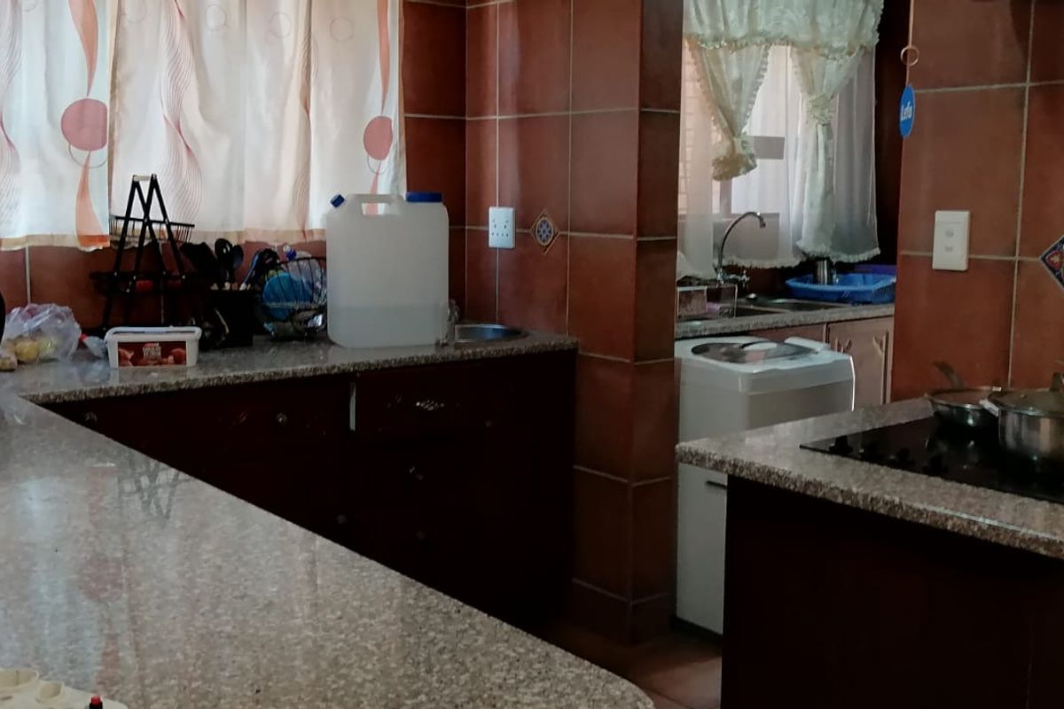 A functional kitchen featuring dark wood cabinetry, granite countertops, and ceramic wall tiling, with an integrated electric hob and a separate scullery area.