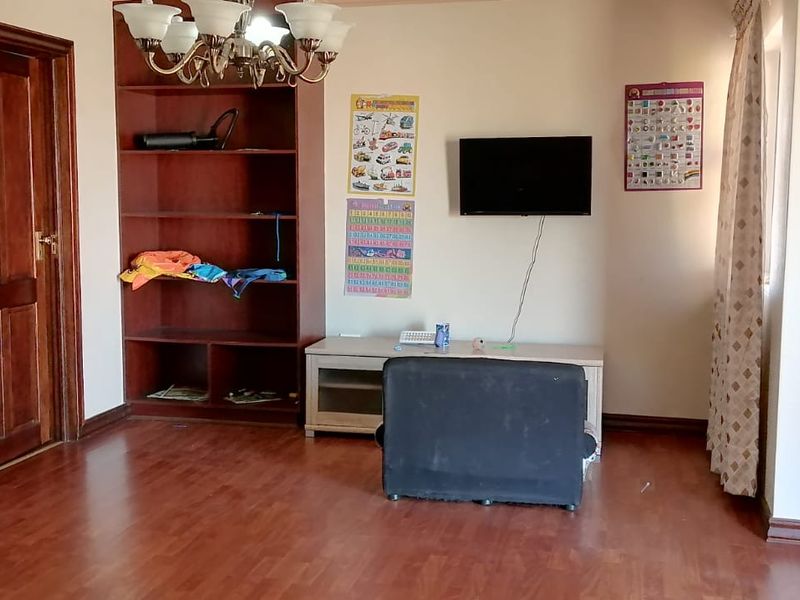 A living room featuring laminate flooring, a built-in timber shelving unit, and a decorative leaded glass door.