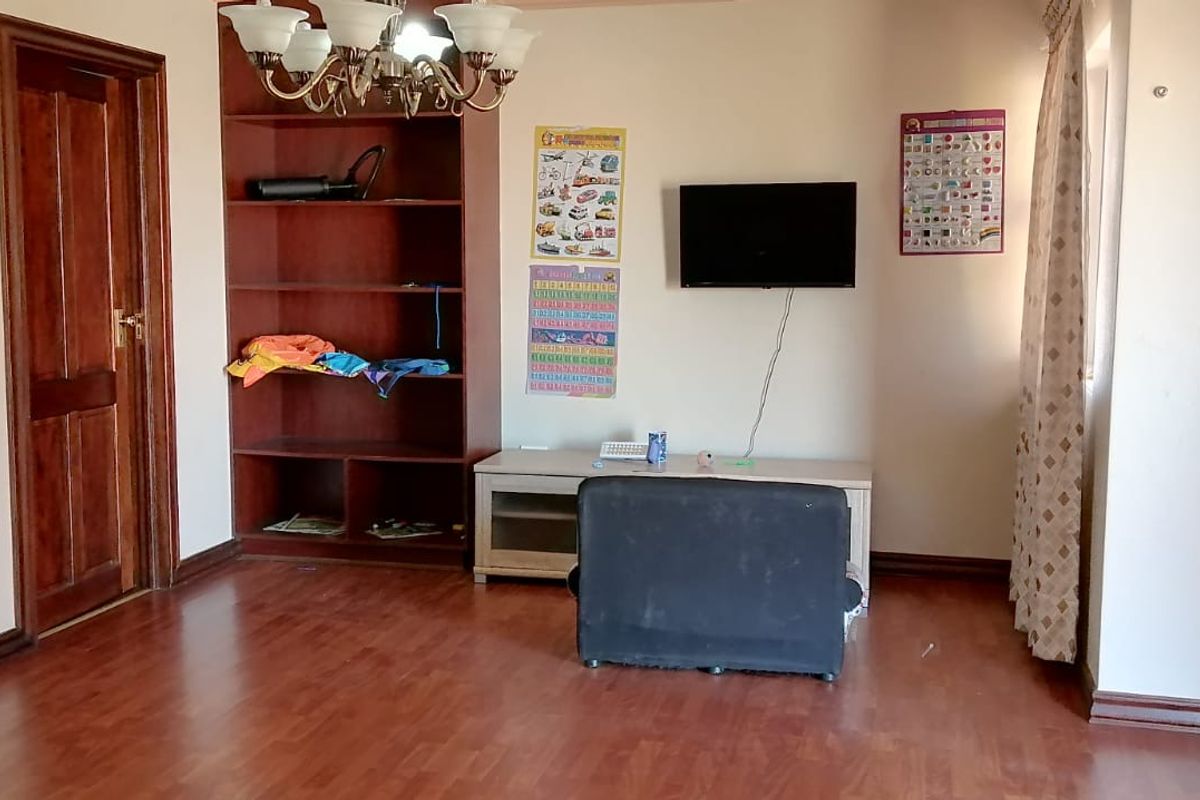 A living room featuring laminate flooring, a built-in timber shelving unit, and a decorative leaded glass door.