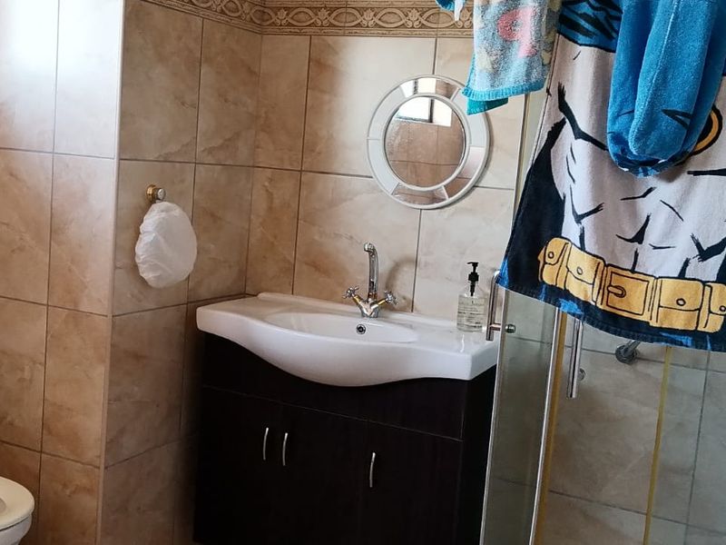 A functional bathroom featuring a vanity cabinet with a basin, a toilet, and a glass-enclosed shower, finished with neutral wall tiles.