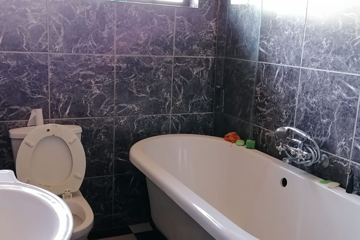 A functional bathroom featuring a classic freestanding bathtub, wall-mounted fixtures, and dark marble-effect wall tiling.