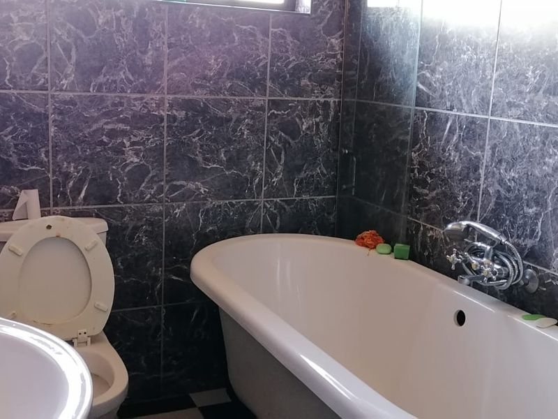A functional bathroom featuring a classic freestanding bathtub, wall-mounted fixtures, and dark marble-effect wall tiling.