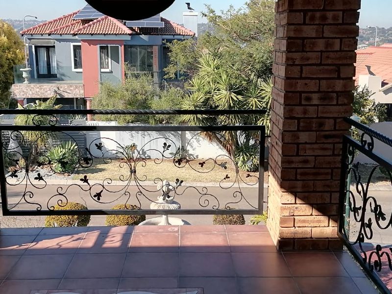 A covered balcony featuring decorative wrought iron balustrades, sturdy brick pillars, and tiled flooring, offering an elevated view of the surrounding residential neighborhood.