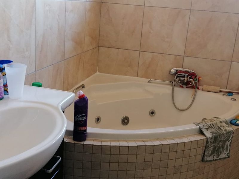 A functional bathroom featuring a corner bathtub with integrated jets, a vanity basin with a mixer tap, and neutral wall and floor tiling.