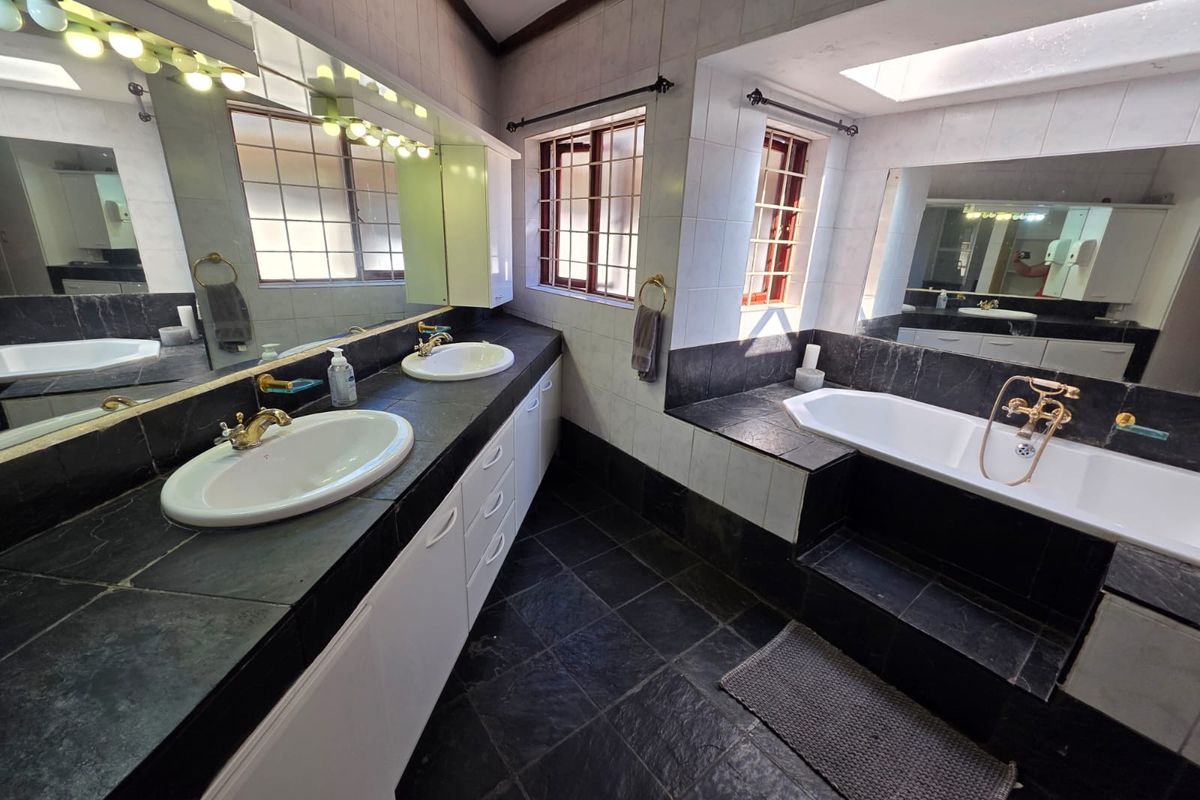 Spacious bathroom featuring a dual vanity with stone countertops, a built-in bathtub, and large mirrors, finished with dark slate-style floor and wall tiles.