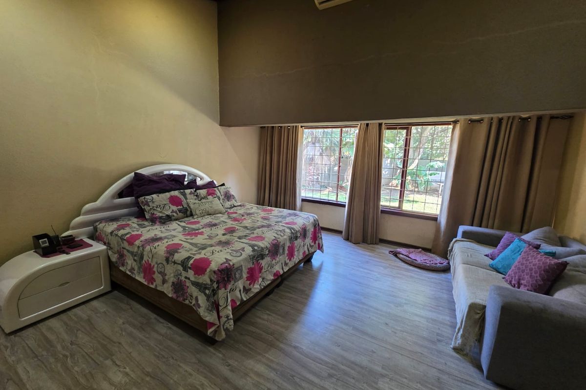 Spacious bedroom featuring wood-look laminate flooring, large windows with garden views, and a wall-mounted air conditioning unit.