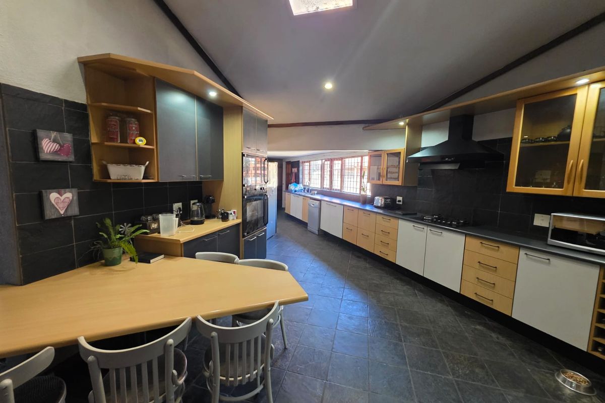 Spacious kitchen featuring extensive cabinetry, built-in oven, extractor fan, and dark tiled flooring with a breakfast nook area.