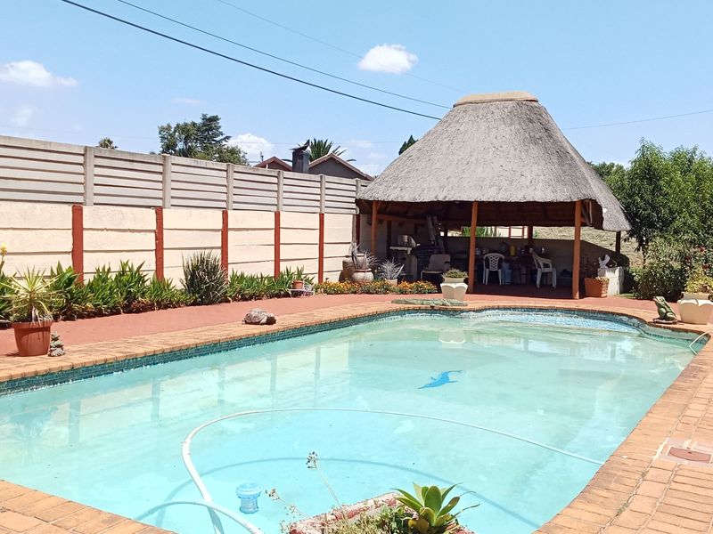 Outdoor pool area featuring a swimming pool with brick coping and a thatched-roof lapa entertainment space.