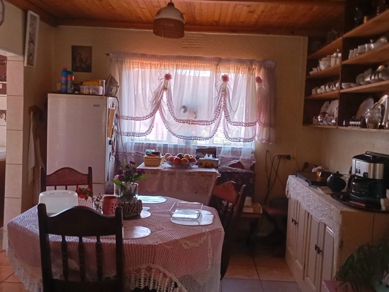 A dated kitchen featuring timber ceiling paneling, open shelving, and tiled flooring, offering a functional space with potential for modernization.