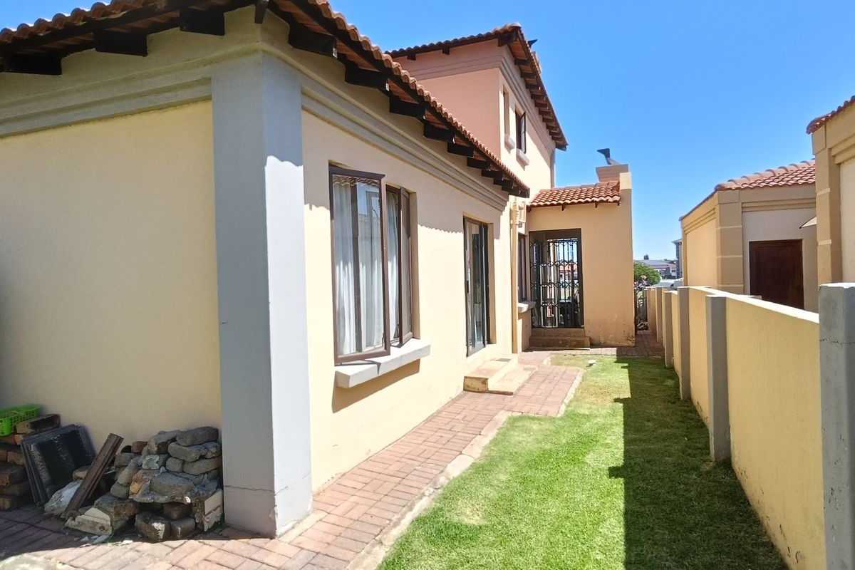 A view of the side exterior of the house featuring a paved walkway, small lawn area, and perimeter boundary wall.