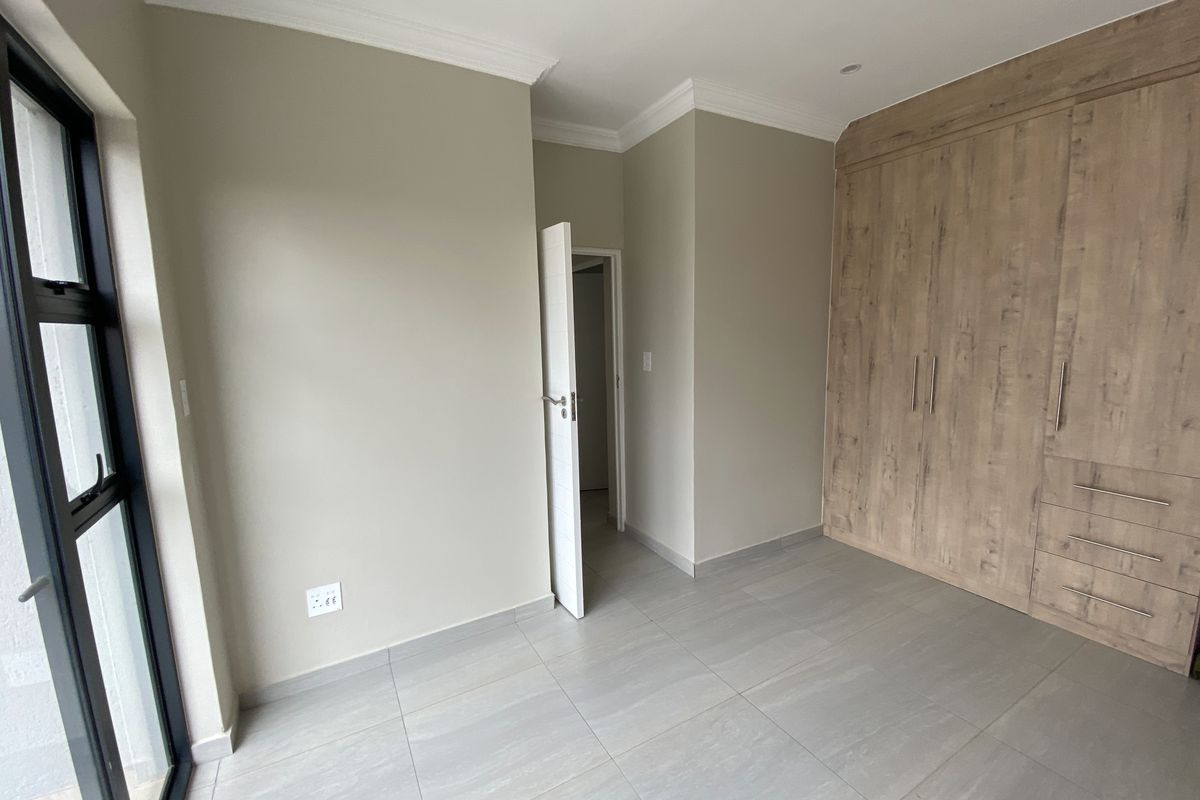 A bright bedroom featuring modern light grey floor tiles, neutral wall paint, crown molding, and built-in wooden cabinetry with integrated drawers.
