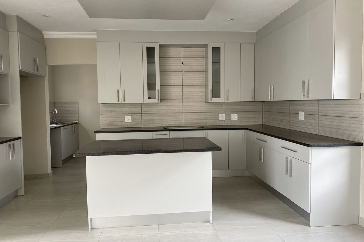 Modern kitchen featuring light grey cabinetry, dark granite countertops, a central island, and tiled backsplash, with an adjacent scullery area.