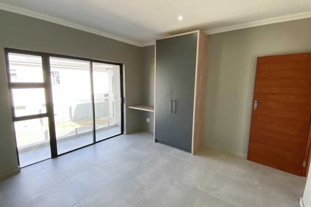 A bright bedroom featuring large sliding glass doors, neutral tiled flooring, and a built-in wardrobe with an integrated desk area.