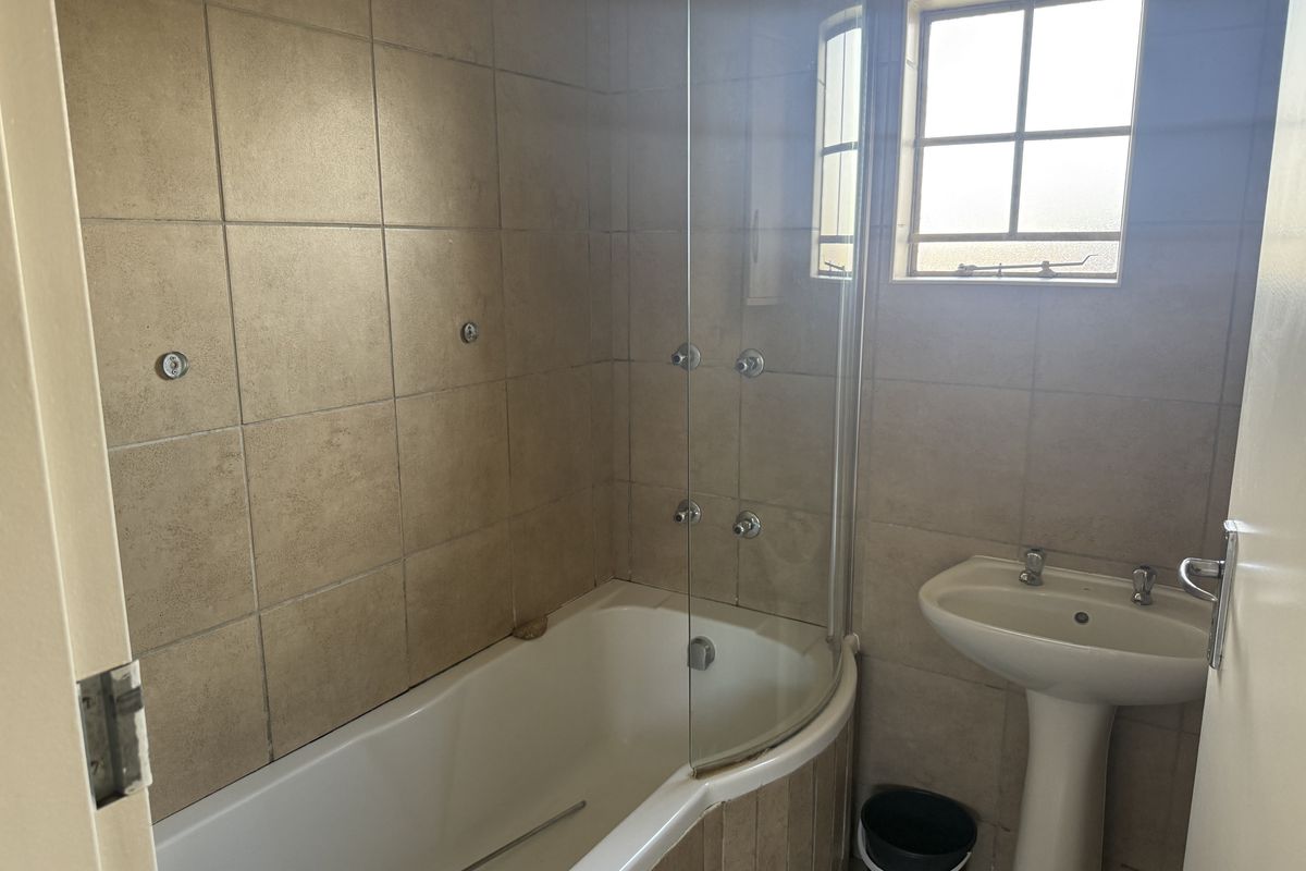 A functional bathroom featuring a bathtub with a glass shower screen, a pedestal basin, and tiled walls.