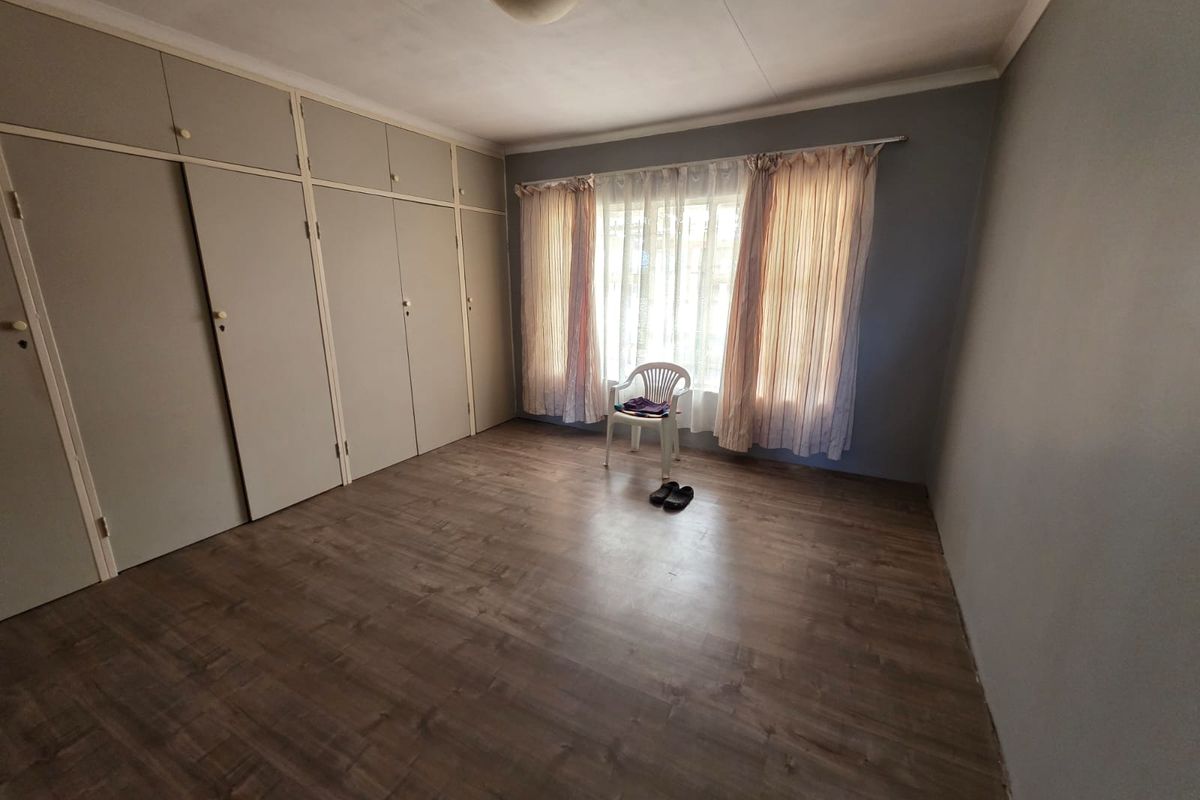 A spacious bedroom featuring extensive built-in floor-to-ceiling cabinetry, wood-look laminate flooring, and large windows with natural light.