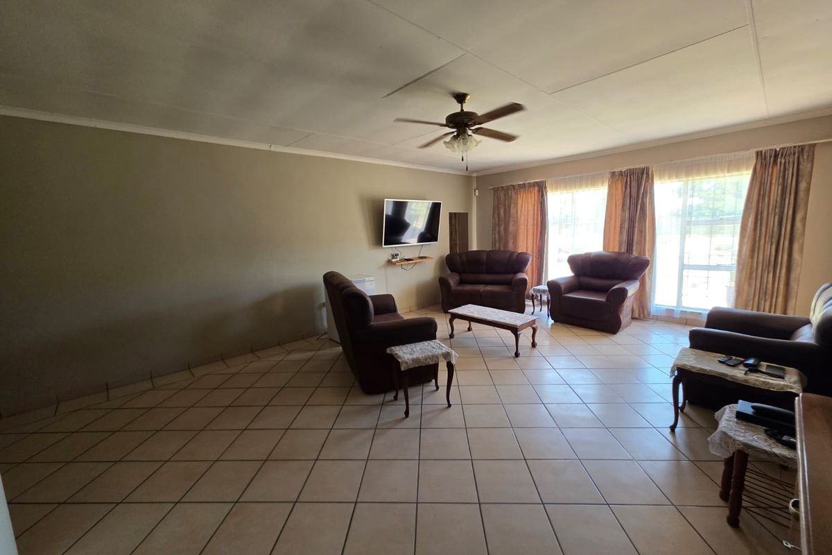 Spacious living room featuring large format floor tiles, a ceiling fan, and expansive windows allowing for natural light.