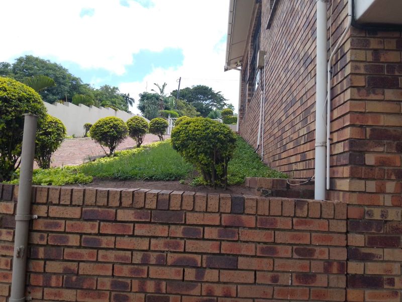 A view of the property's brick facade, featuring a well-maintained retaining wall and landscaped garden area along the side of the house.