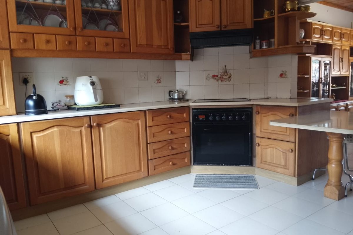 A traditional kitchen featuring extensive wooden cabinetry, built-in oven, extractor fan, and tiled flooring, offering a functional layout with ample storage space.