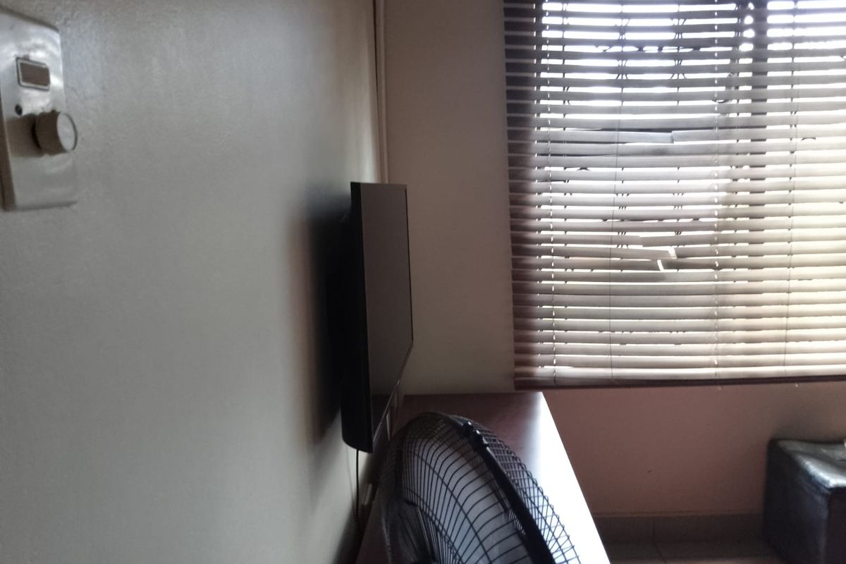 A bedroom interior featuring a window with venetian blinds and a wall-mounted light switch.