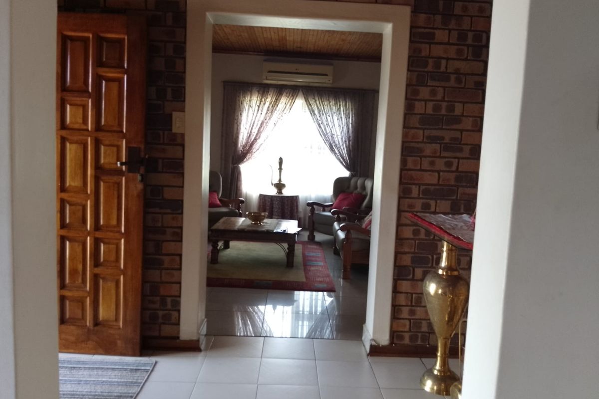 A view from the entryway into a living room featuring exposed brick walls, tiled flooring, and a timber ceiling.
