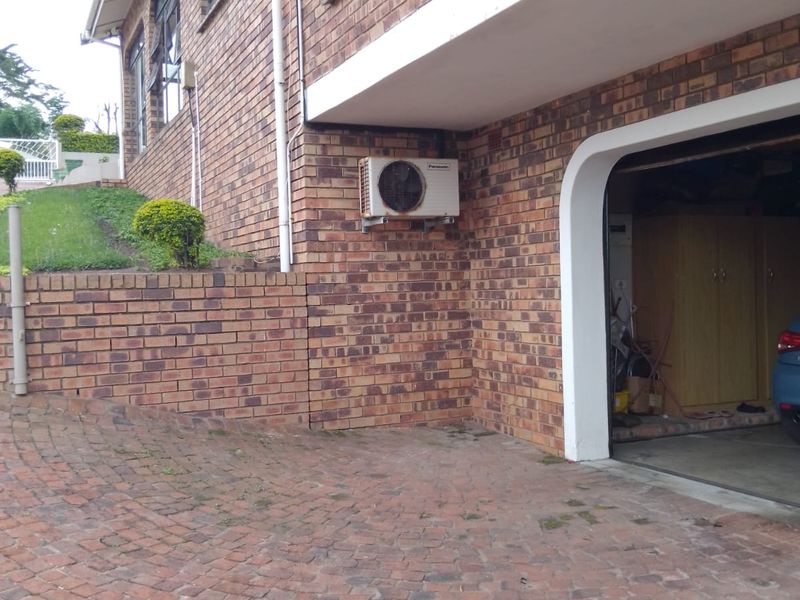 Exterior view of the property featuring a brick facade, paved driveway, retaining wall, and an integrated garage with an external air conditioning unit.