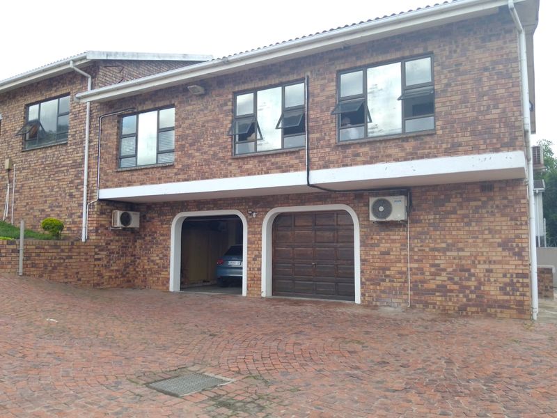 Front elevation of a double-story brick house featuring a double garage, paved driveway, and mounted air conditioning units.