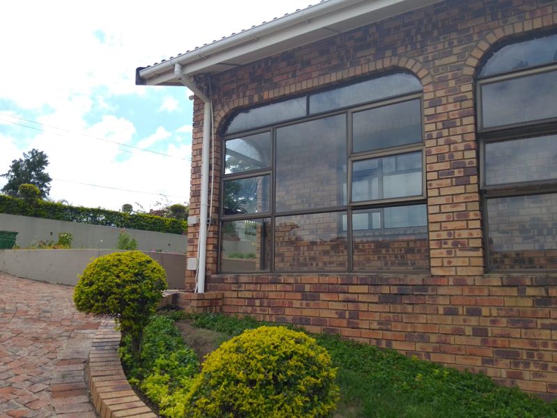 A view of the property's face brick exterior, featuring large aluminium-framed windows, a paved driveway, and well-maintained garden landscaping.