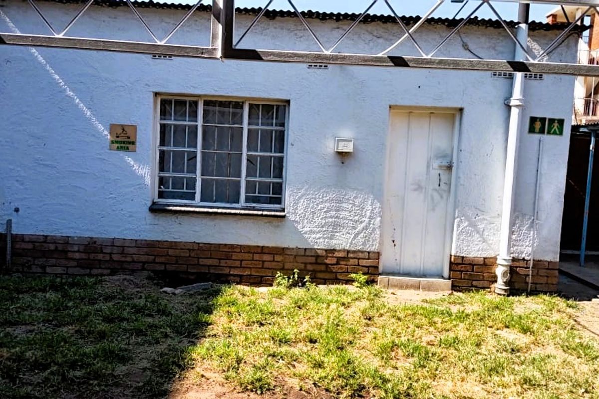 Exterior view of a basic outbuilding featuring a white rendered facade, brick base, and a single entrance door with a window.