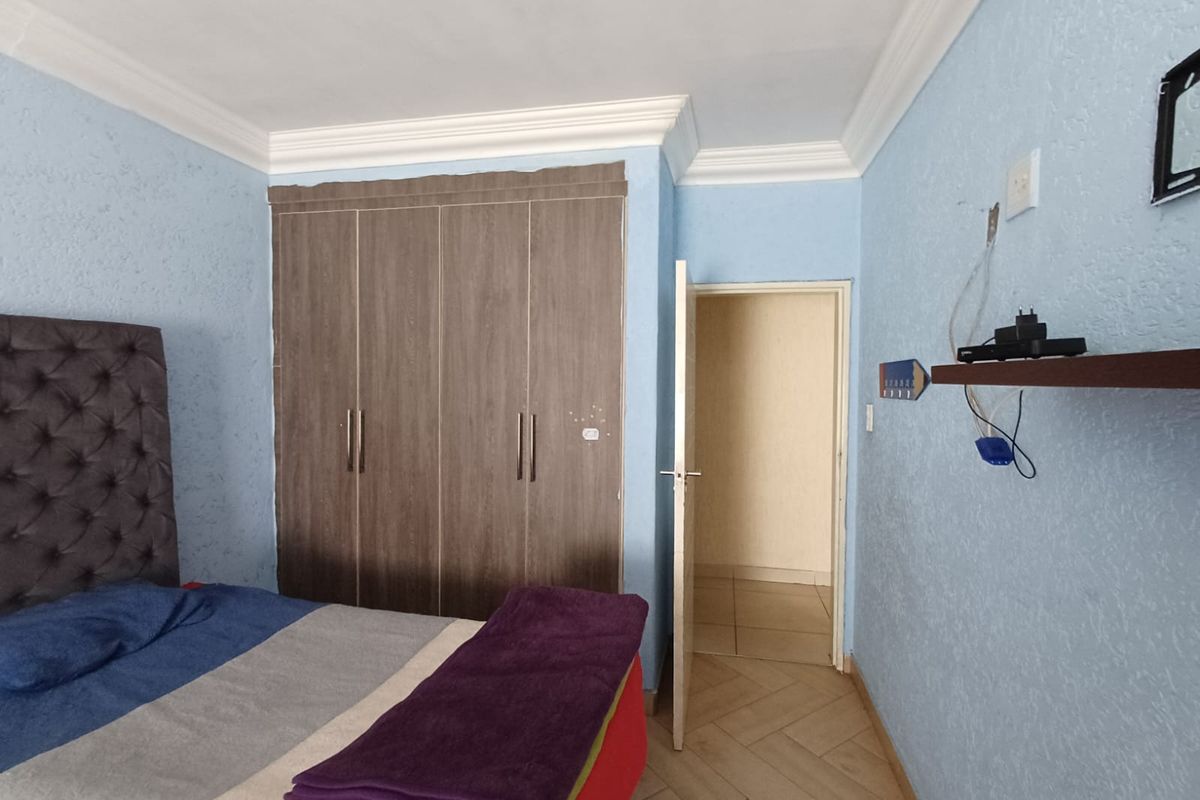 A bedroom featuring built-in wooden cupboards, crown molding, and tiled flooring, with an open doorway leading to an adjacent space.